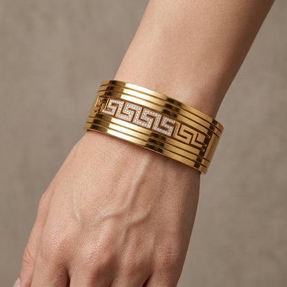 Gold bracelet with intricate design on a wrist against a neutral background