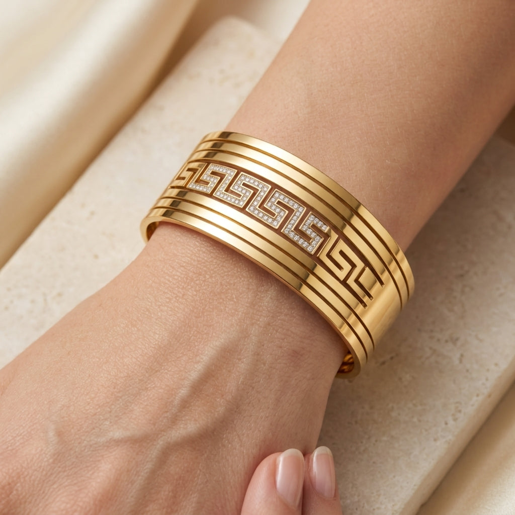 Gold bracelet with intricate design on a wrist against a beige background