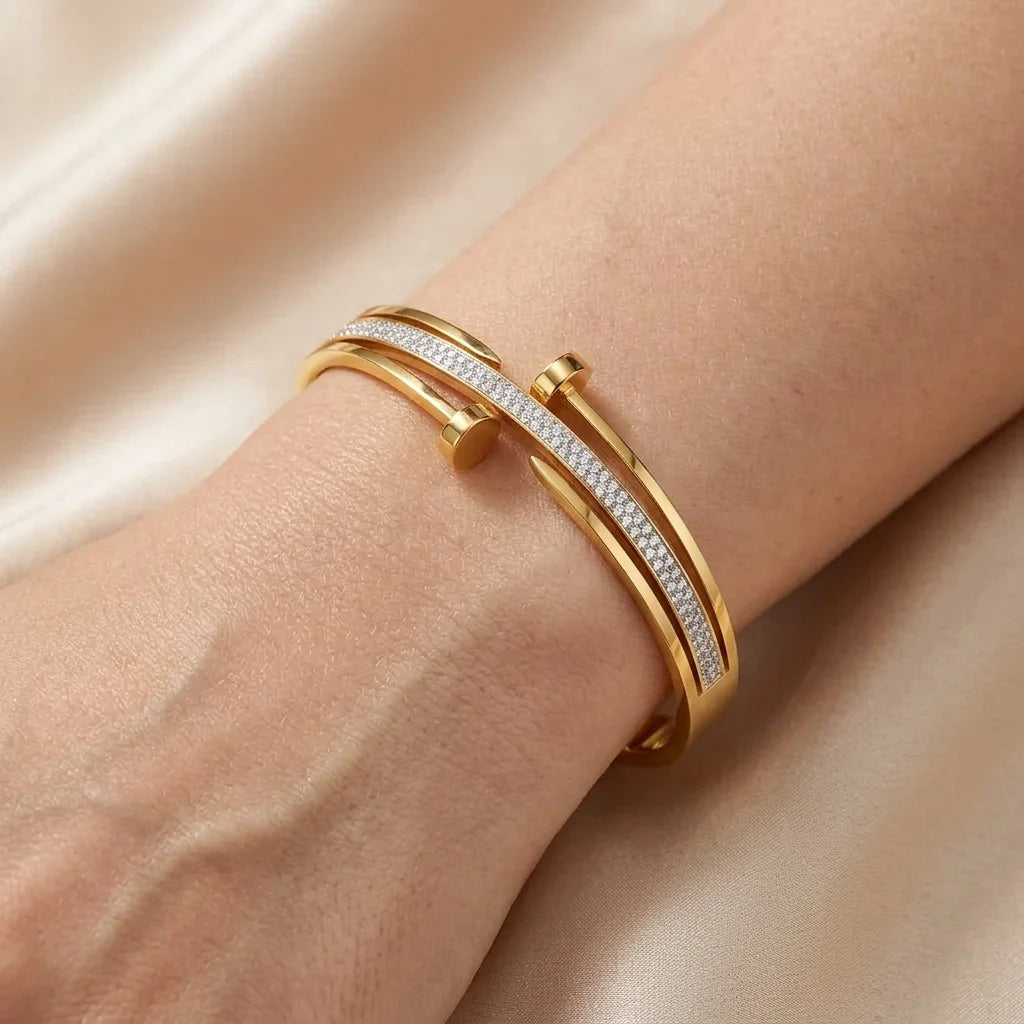 Gold bracelet with diamond accents on a wrist against a beige background