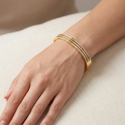 Gold bracelet on a person's wrist against a neutral background