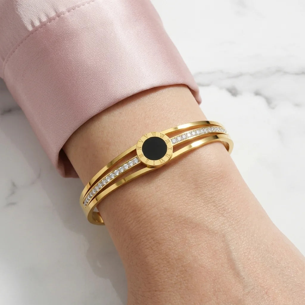 Gold bracelet with a black center stone on a wrist against a marble background