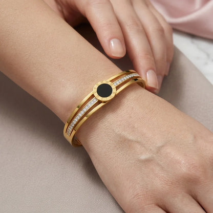 Gold bracelet with a black center stone on a wrist against a neutral background