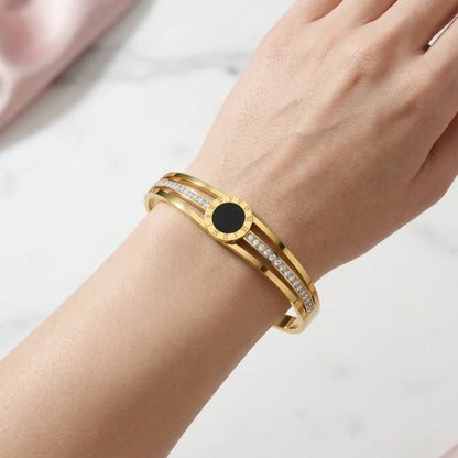 Gold bracelet with a black center on a wrist against a light background