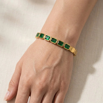 Gold bracelet with green gemstones on a wrist against a neutral background
