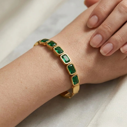 Gold bracelet with green gemstones on a wrist against a neutral background