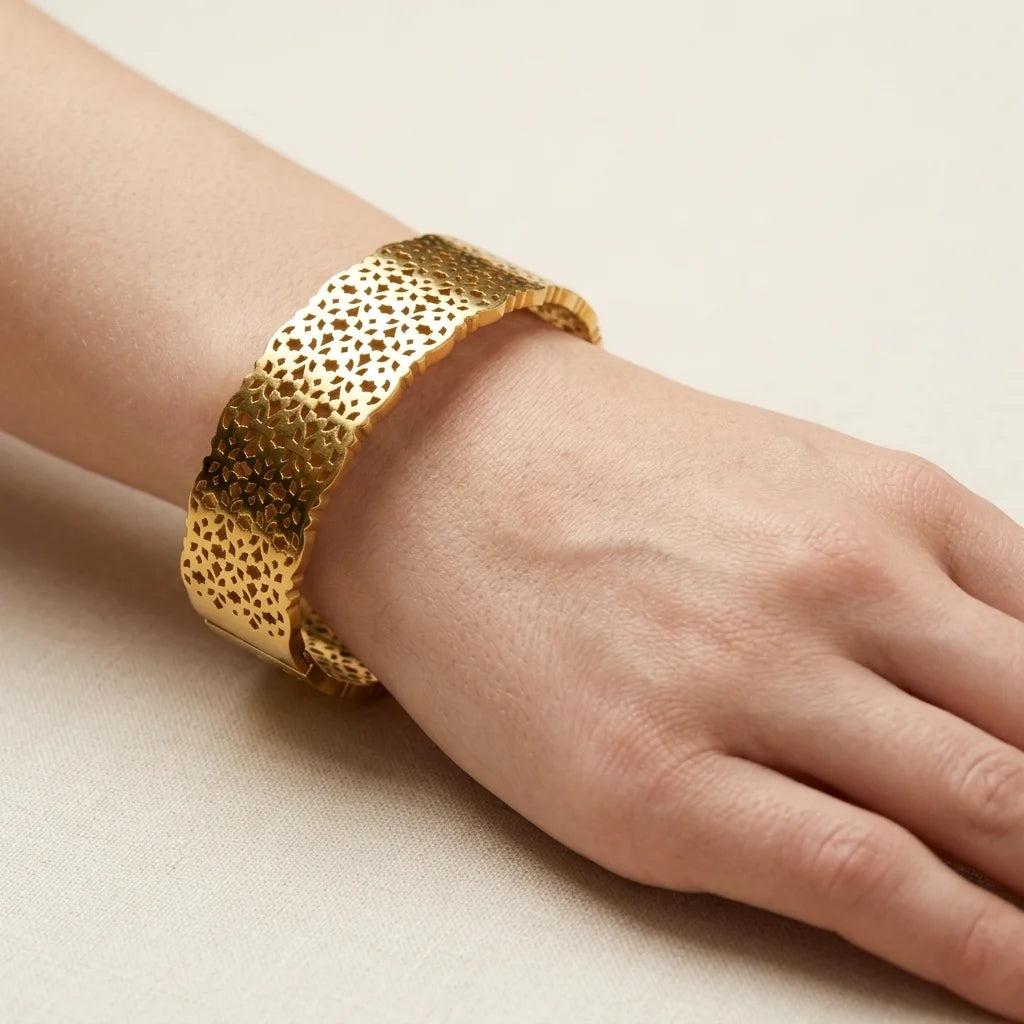 Gold textured bracelet on a wrist against a beige background