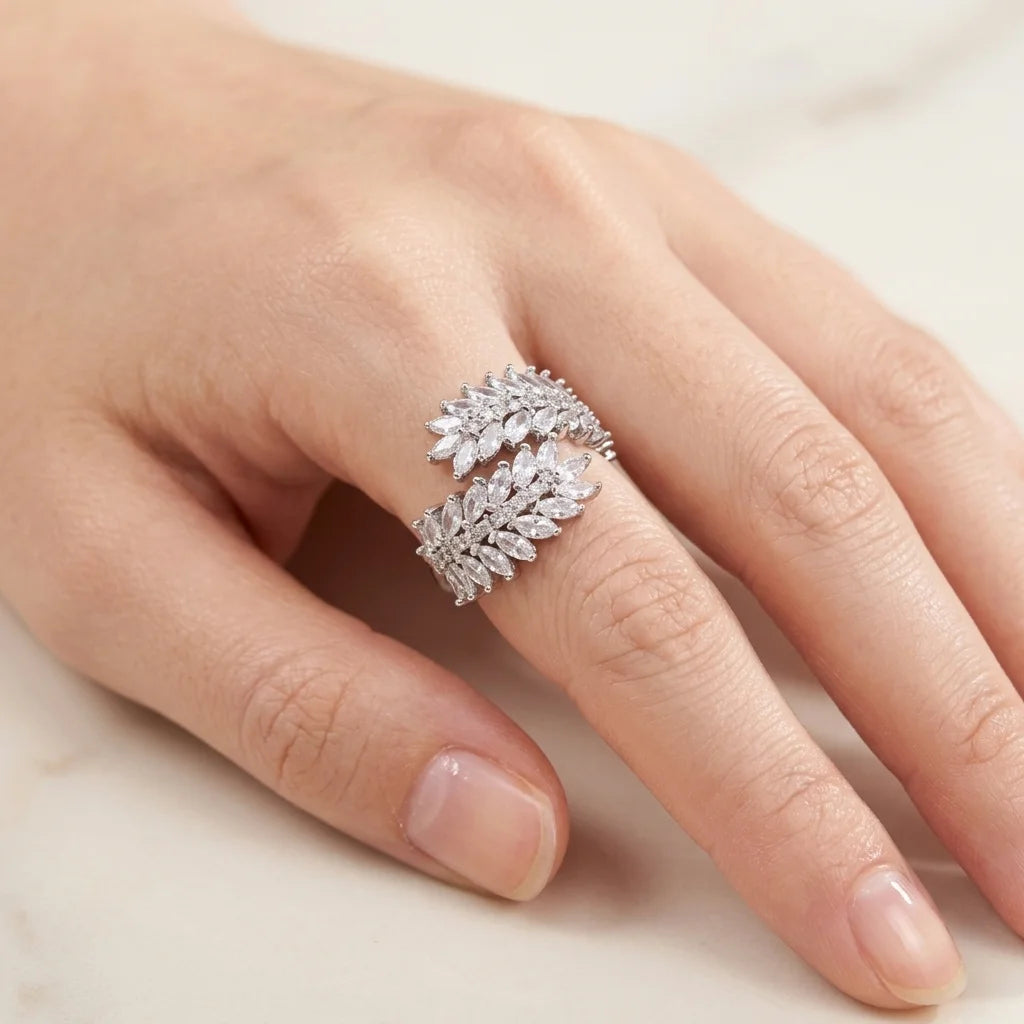 Close-up of a hand wearing a silver ring with diamond-like stones on a neutral background