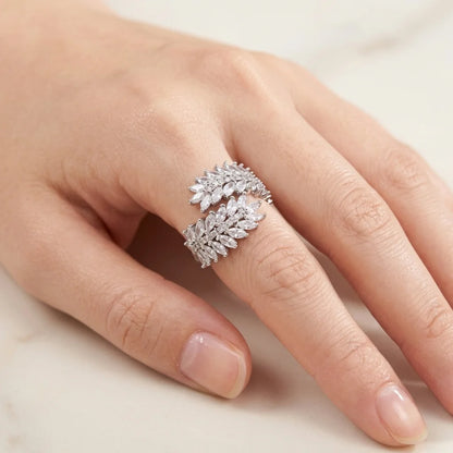 Close-up of a hand wearing a silver ring with diamond-like stones on a neutral background