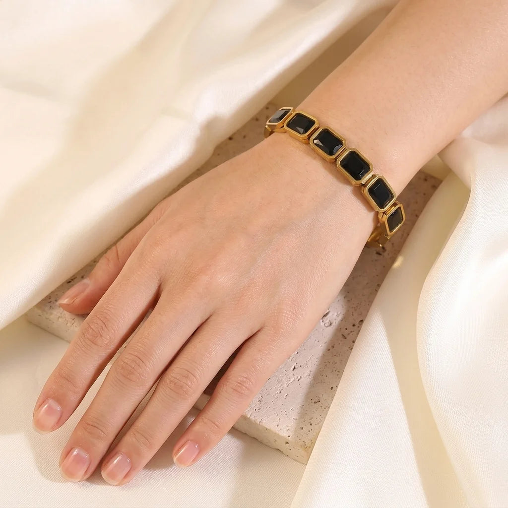 Gold bracelet with black stones on a hand against a neutral background