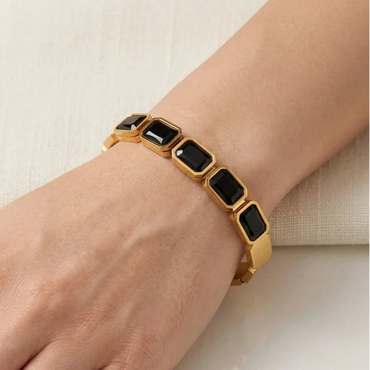 Gold bracelet with black stones on a hand against a neutral background