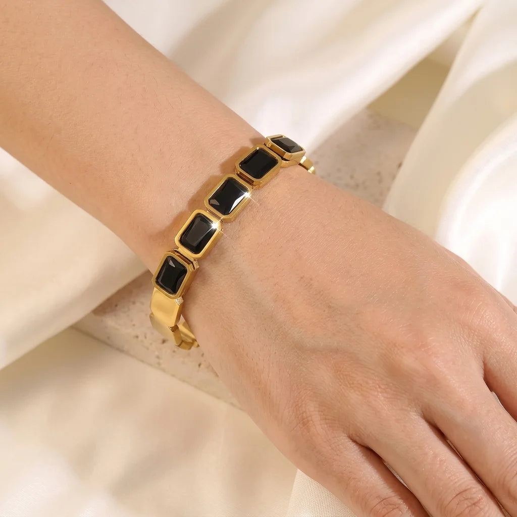 Gold bracelet with black stones on a wrist against a white background