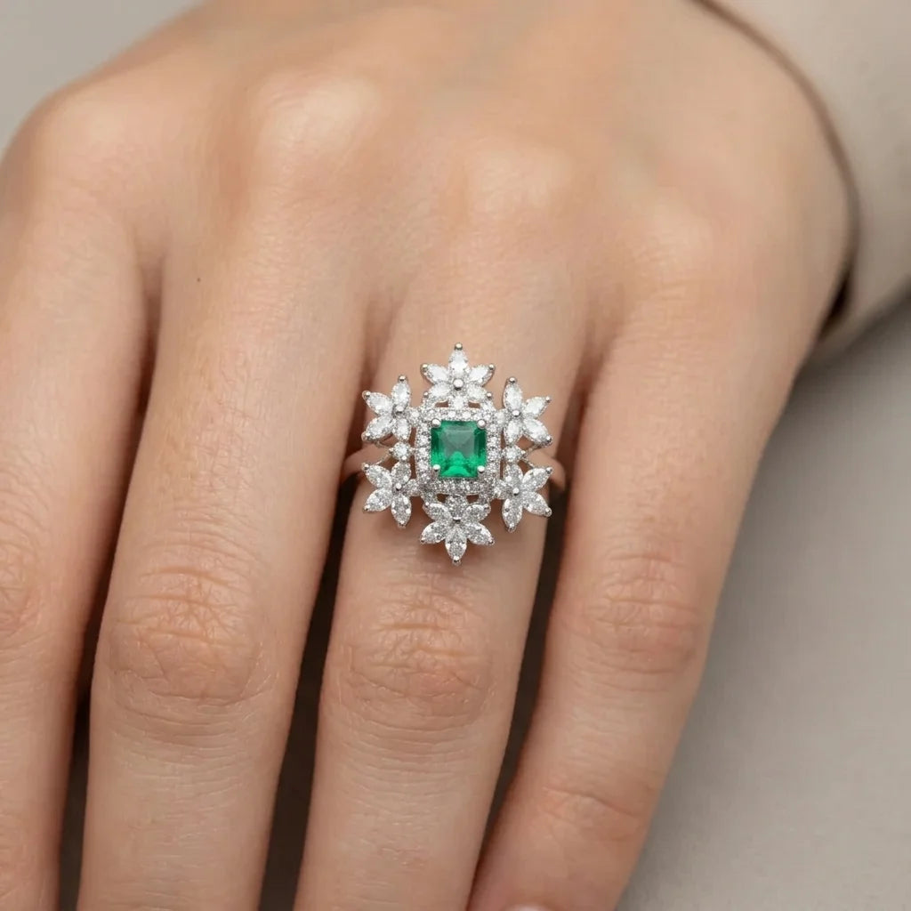 Ring with a green gemstone and diamond-like stones on a finger against a neutral background