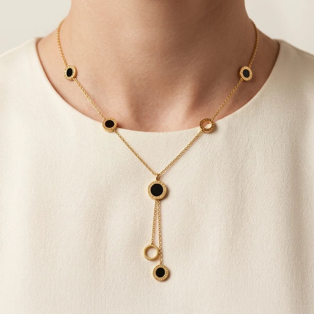 Gold necklace with black stones worn by a person on a beige background