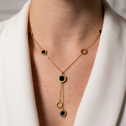 Gold necklace with black stones worn by a person in a white outfit