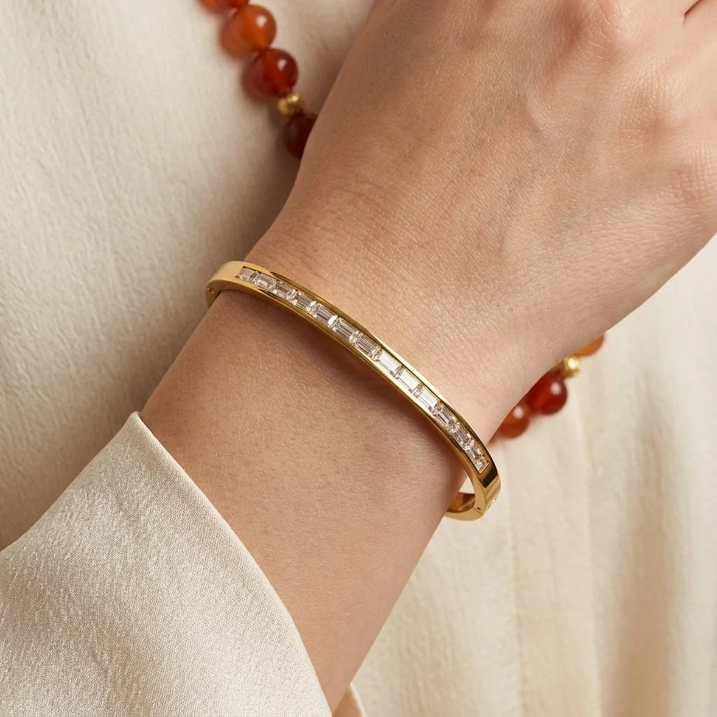 Gold bracelet with gemstones on a wrist against a neutral background