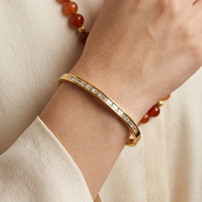 Gold bracelet with gemstones on a wrist against a neutral background