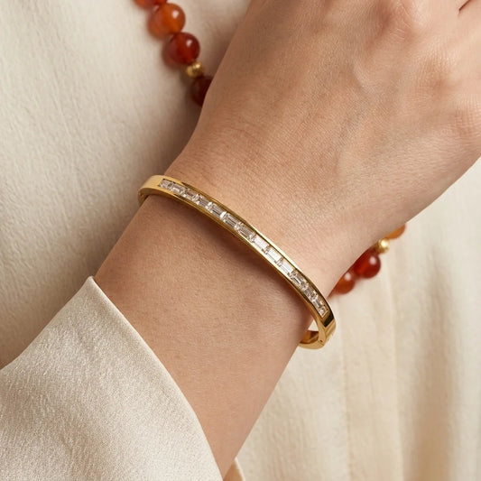 Gold bracelet with gemstones on a wrist against a neutral background