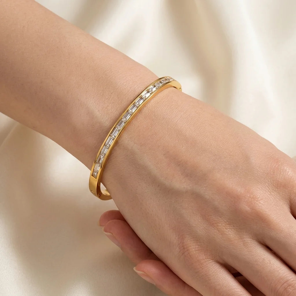 Gold bracelet with clear stones on a wrist against a neutral background