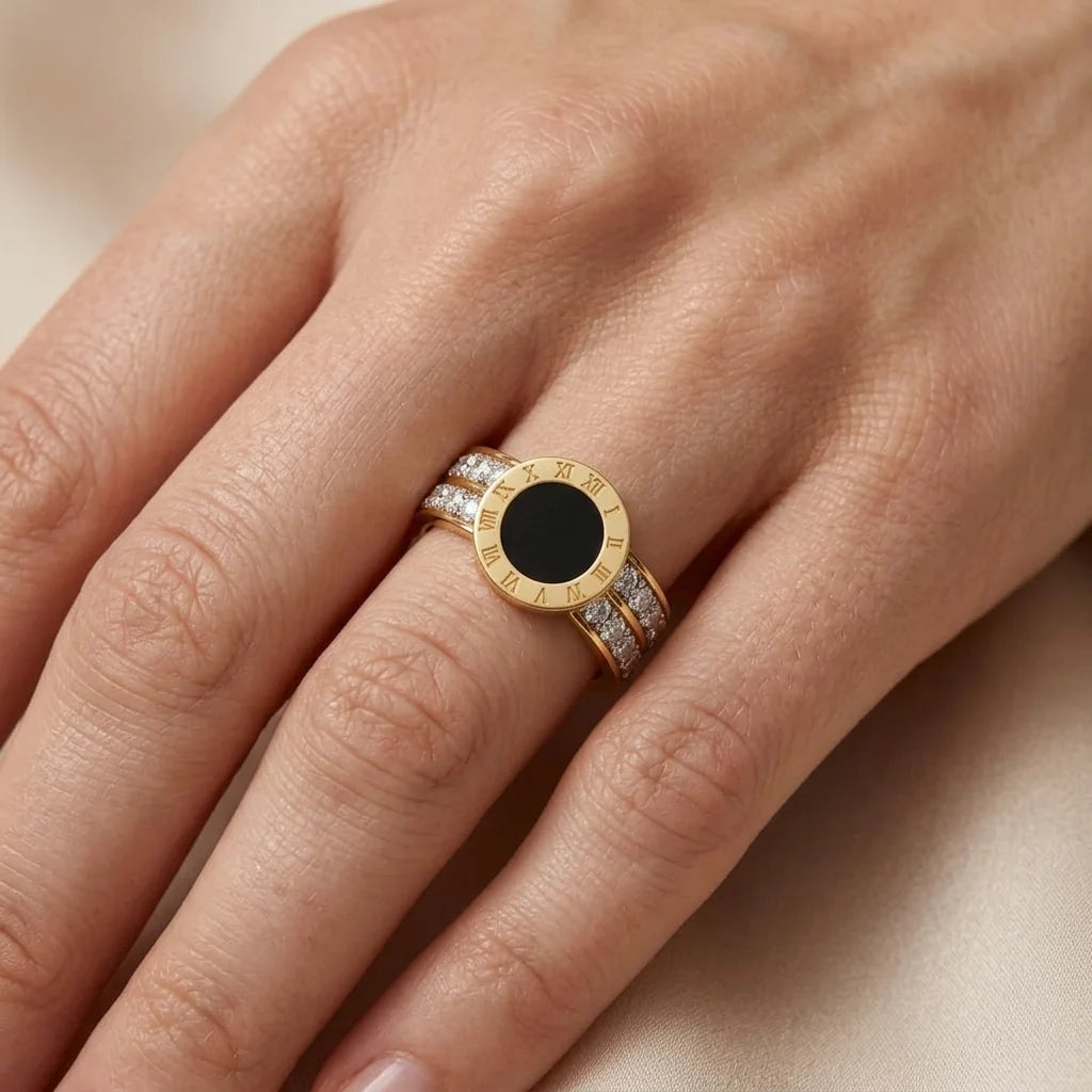 Gold ring with a black gemstone on a hand against a neutral background