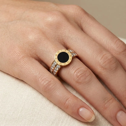 Gold ring with a black gemstone on a person's finger against a beige background