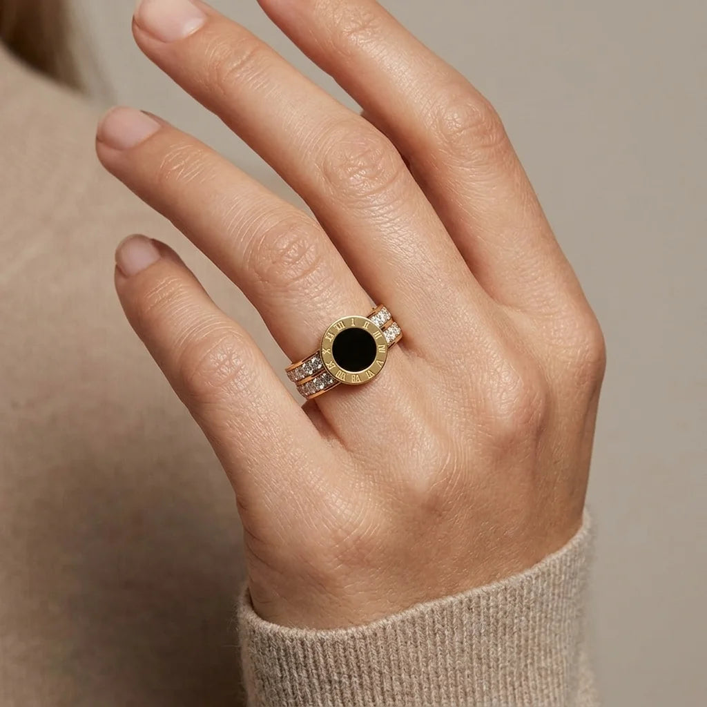 Hand wearing a gold ring with a black gemstone on a neutral background