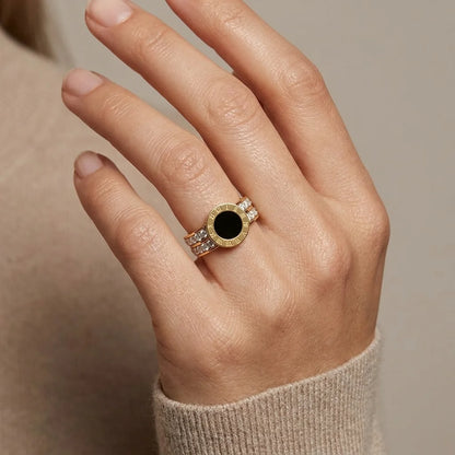 Hand wearing a gold ring with a black gemstone on a neutral background
