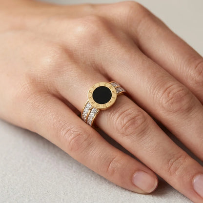 Gold ring with a black gemstone on a person's finger against a neutral background