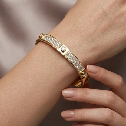 Gold bracelet with gemstones on a wrist against a neutral background