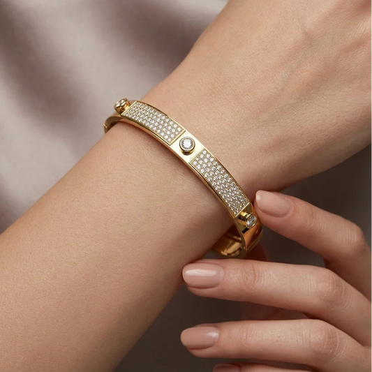 Gold bracelet with gemstones on a wrist against a neutral background