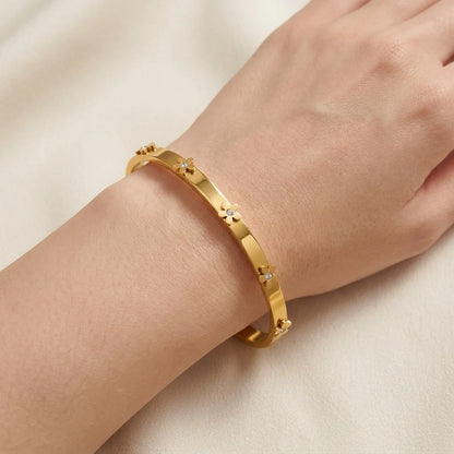 Gold bracelet with star-shaped stones on a wrist against a beige background