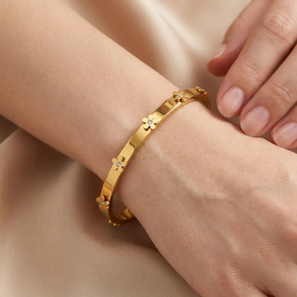 Gold bracelet with floral designs on a wrist against a neutral background