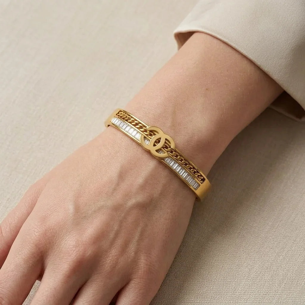 Gold bracelet with a brand logo on a beige background