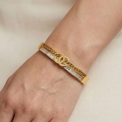Gold bracelet with chain design on a wrist against a neutral background