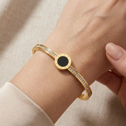 Gold bracelet with a black center on a wrist against a beige background