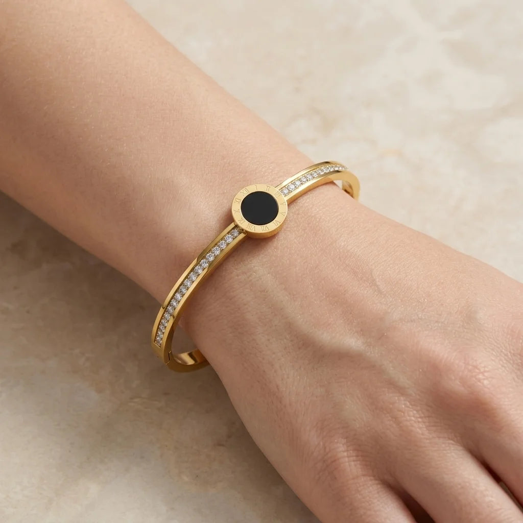 Gold bracelet with a black center stone on a wrist against a beige background