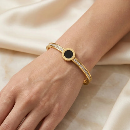Gold bracelet with a black center stone on a wrist against a beige fabric background