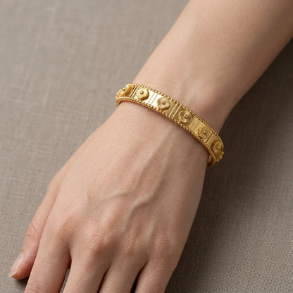 Gold bracelet on a wrist against a neutral background