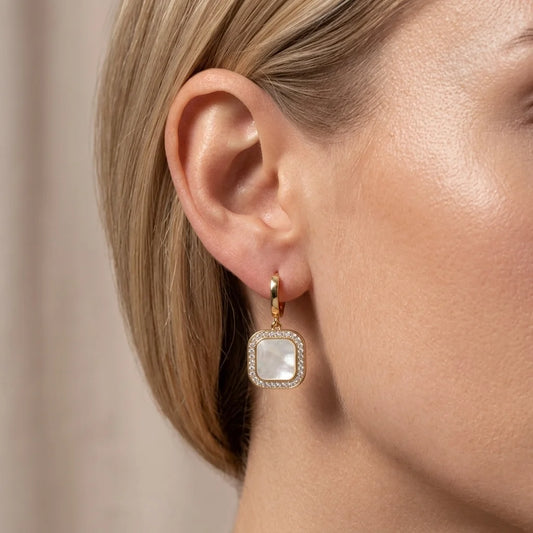 Gold earring with a square gemstone worn by a person with blonde hair.