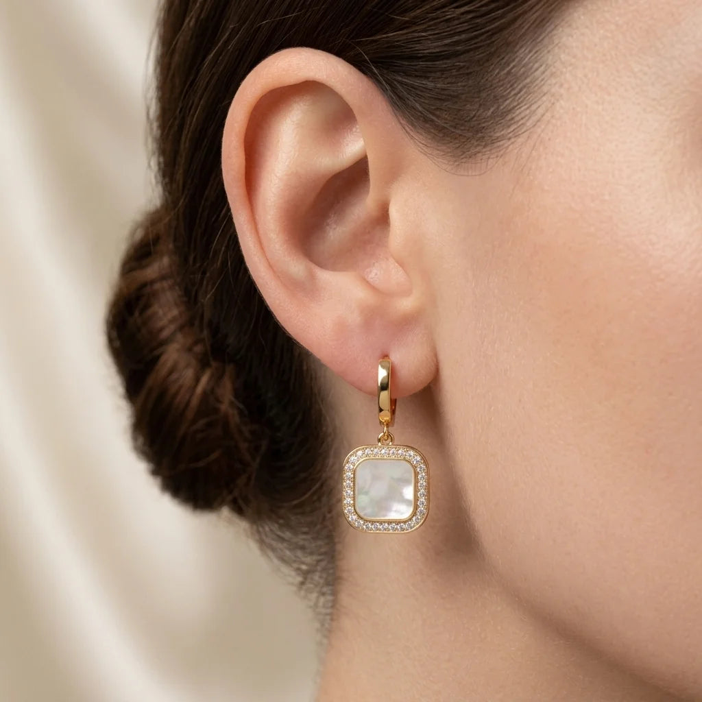 Gold earring with a clear gemstone worn by a person, blurred background