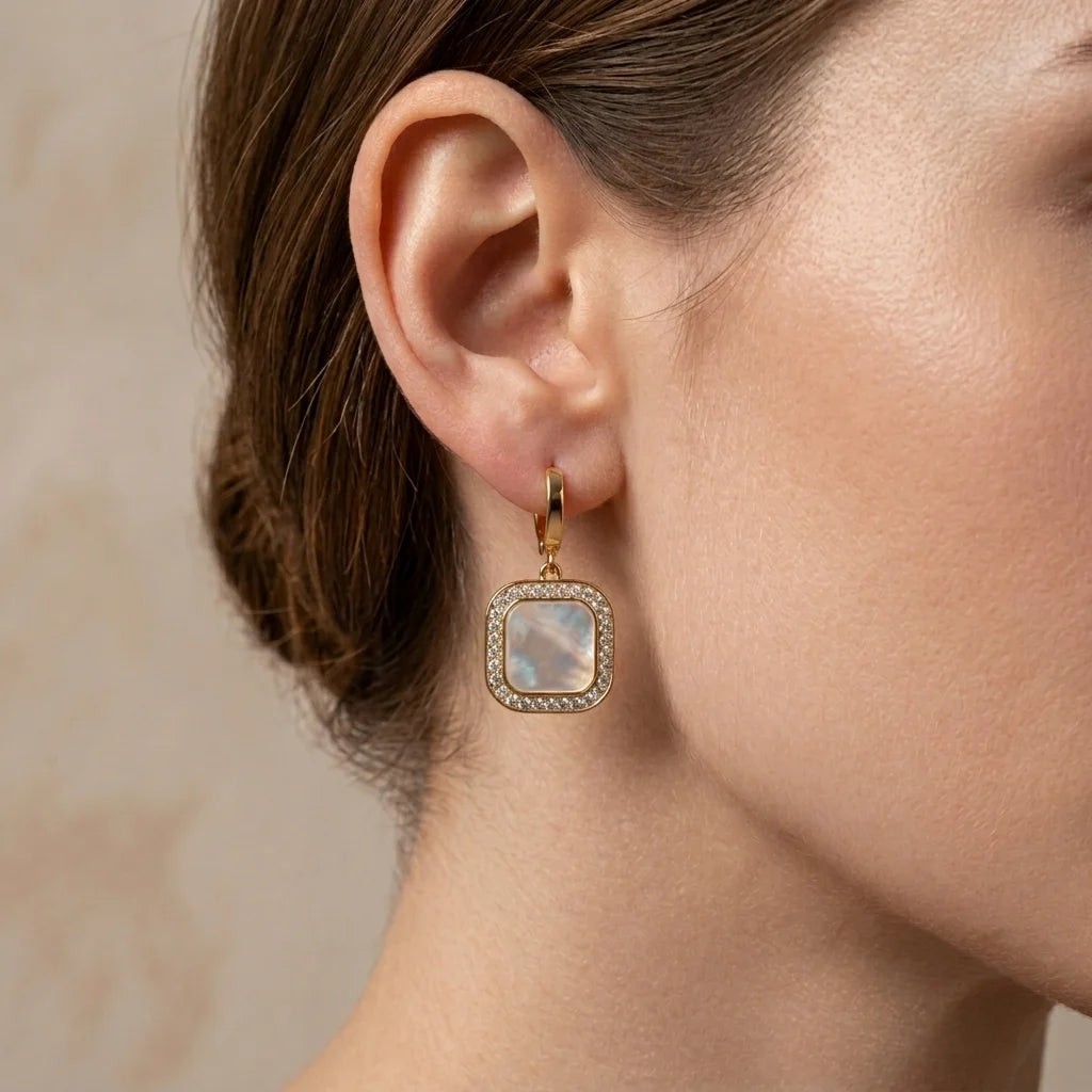 Close-up of an ear wearing a gold earring with a gemstone on a neutral background
