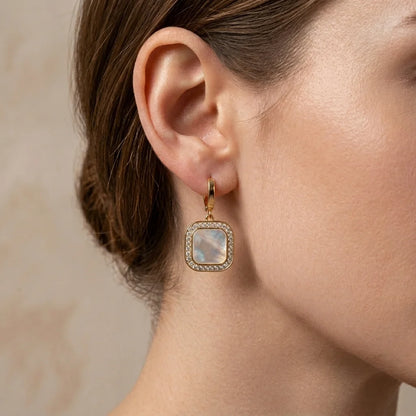 Close-up of an ear wearing a gold earring with a gemstone on a neutral background