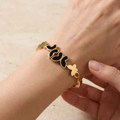 Gold bracelet with black heart charms on a wrist against a beige background