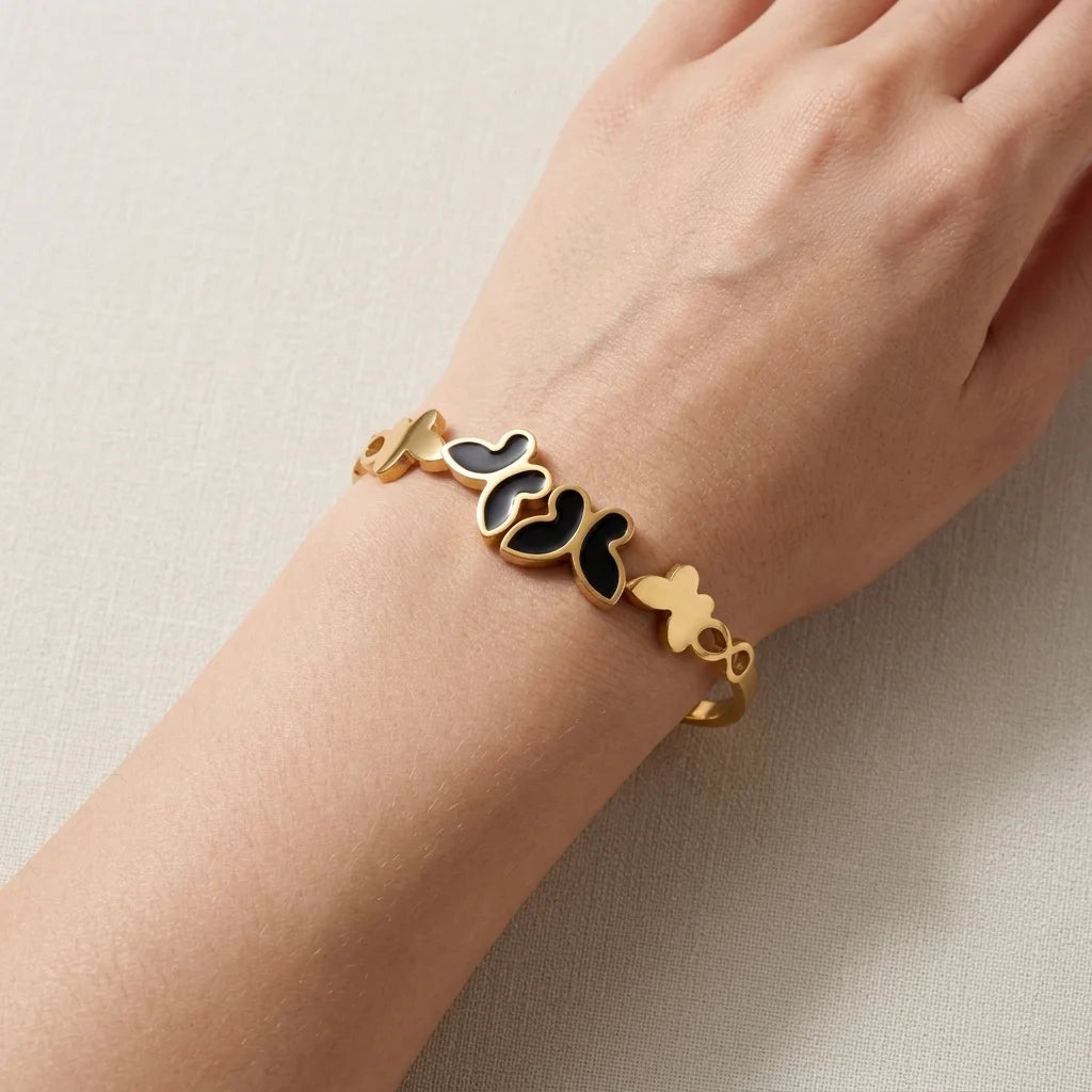 Gold bracelet with black heart charms on a wrist against a beige background