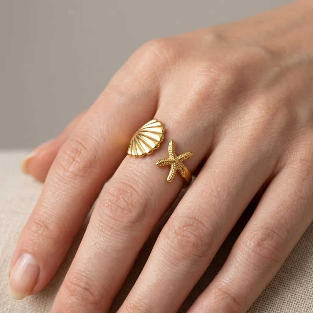Gold shell and starfish ring on a hand against a neutral background