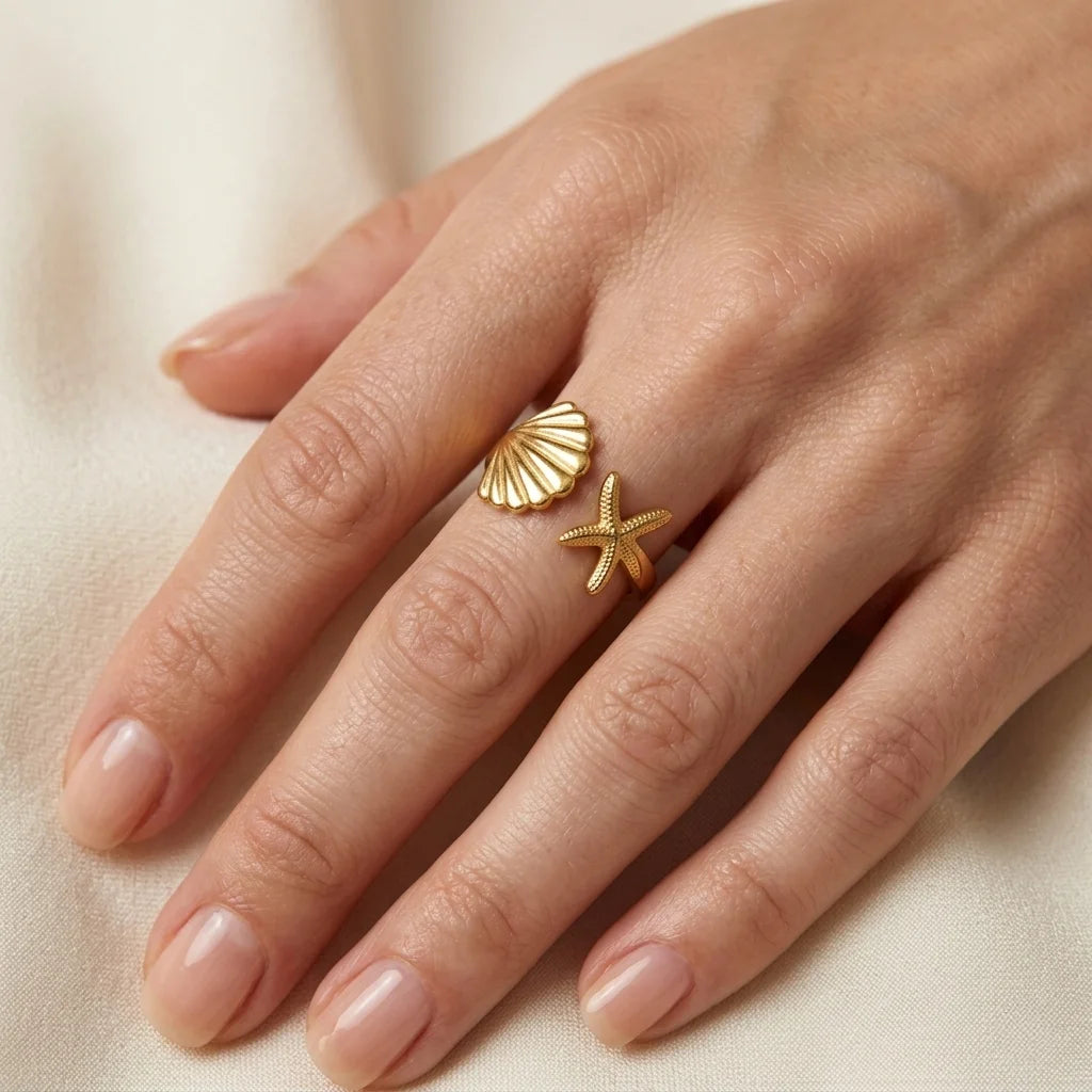 Gold shell and starfish ring on a hand against a beige background