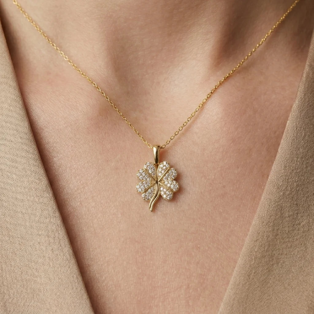 Gold necklace with a clover-shaped pendant on a person wearing a beige top.