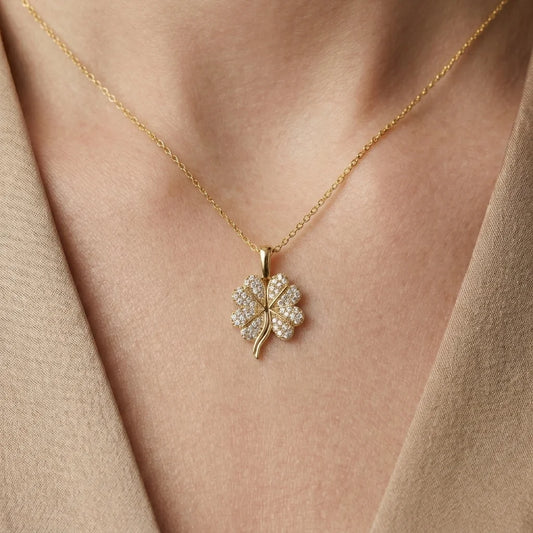 Gold necklace with a clover-shaped pendant on a person wearing a beige top.