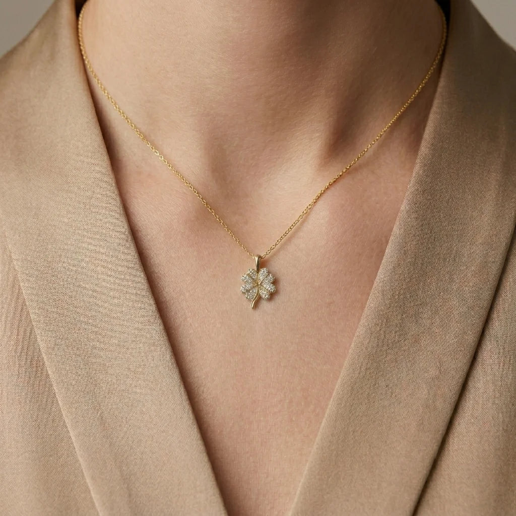 Gold necklace with a clover-shaped pendant worn by a person in a beige outfit.