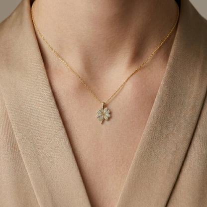 Gold necklace with a clover-shaped pendant worn by a person in a beige outfit.