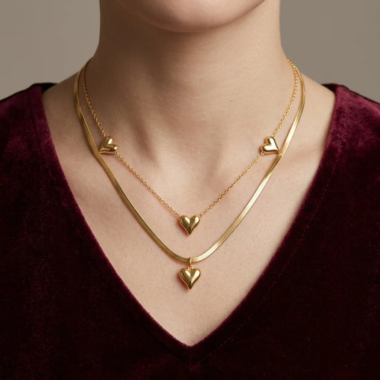 Gold heart-shaped necklace on a person wearing a dark purple top.